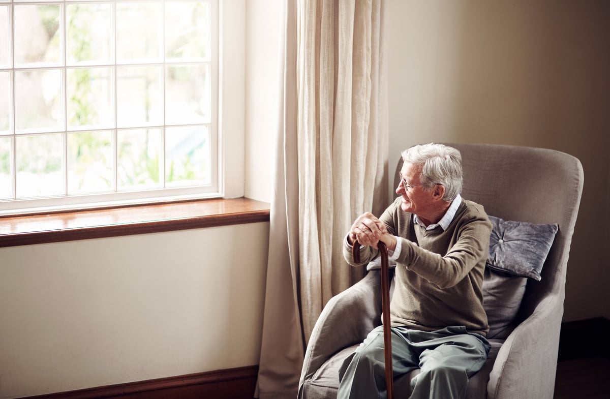 Senior man looking thoughtfully out the window of his own home